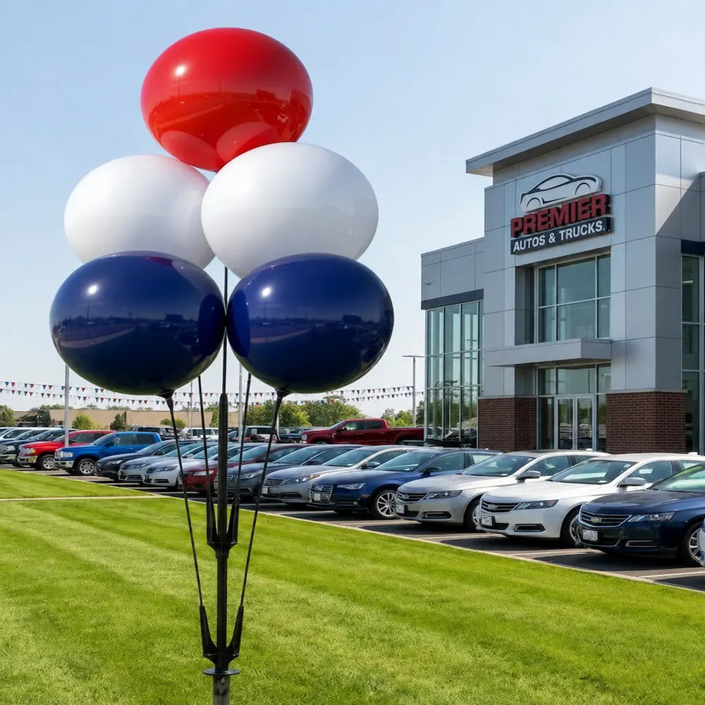 Red, white, and blue  reusable balloons in front of a car dealership with multiple cars on display.